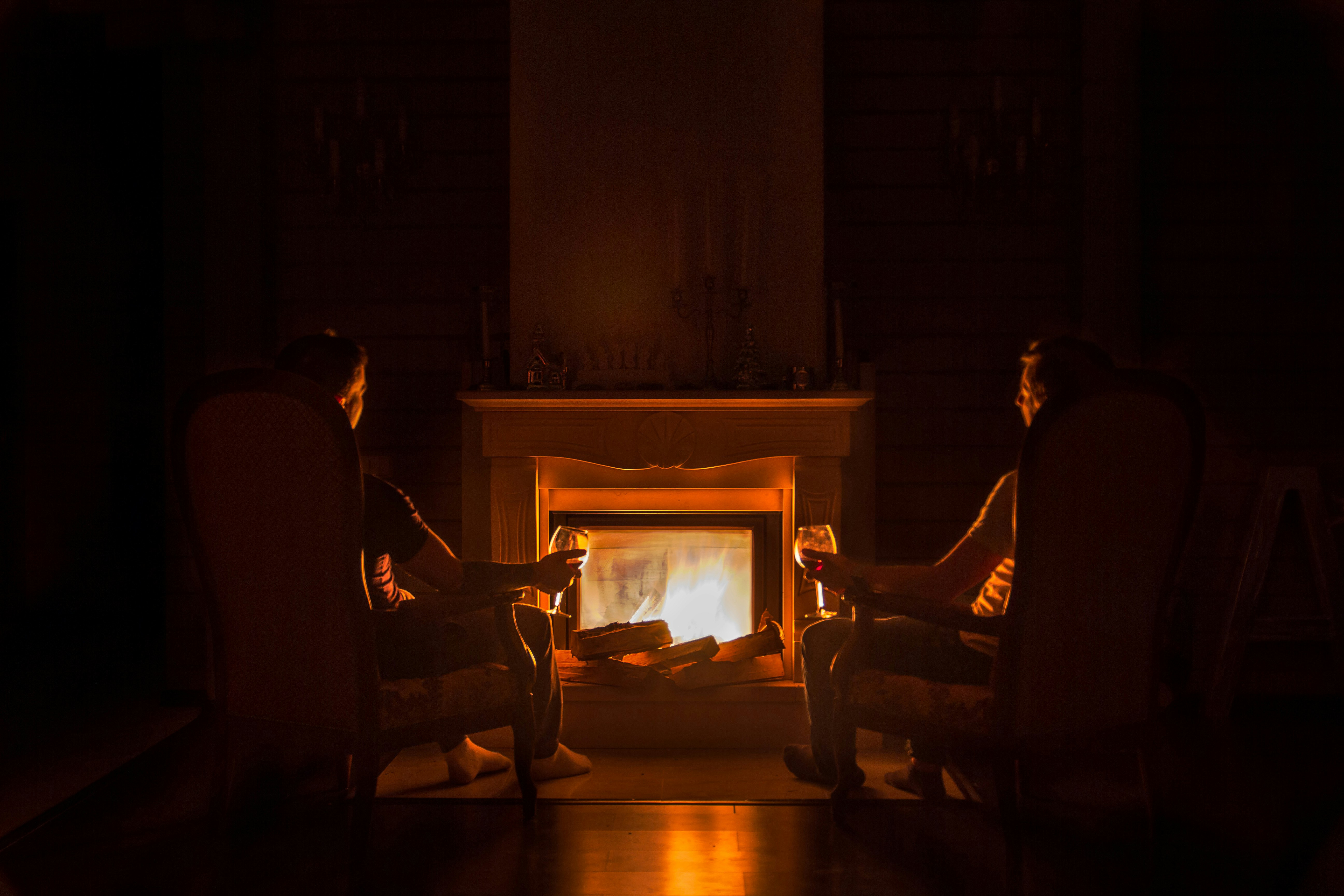 A couple of men sitting by a lit fireplace